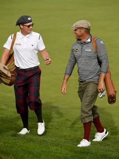 two men walking across a grass covered field holding baseball mitt's and bags