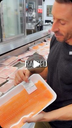 a man is holding a tray of salmon