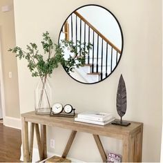 a wooden table topped with a vase filled with flowers next to a mirror on the wall