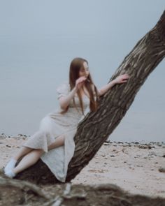 a woman sitting on top of a tree next to the ocean with her hand near her face