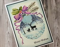 a christmas card with an ornament, holly and a deer in the snow