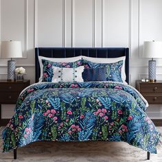 a bed with blue and pink flowers on it in a white room next to two nightstands