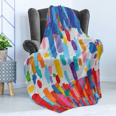 a colorful blanket sitting on top of a chair next to a potted plant in a living room