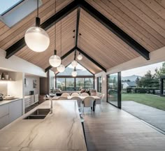 an open kitchen and dining area with wood ceilinging, large windows, and modern lighting fixtures