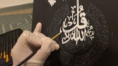 a person in white gloves writing on a piece of black paper with an arabic calligraphy