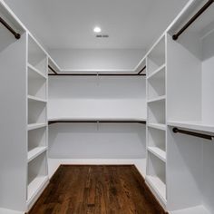 an empty walk - in closet with white shelves and wood flooring on the side