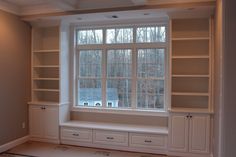 an empty room with built - in bookshelves and drawers on either side of the window