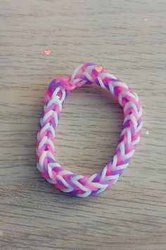 a pink and white braided bracelet on a wooden table with hearts in the background