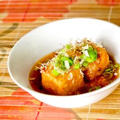 a white bowl filled with food sitting on top of a wooden table next to a bamboo mat