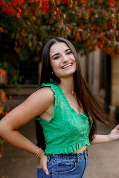 a woman standing in front of a tree with her hands on her hips and smiling at the camera