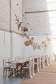 an instagram photo of a long table with white chairs and flowers hanging from the ceiling