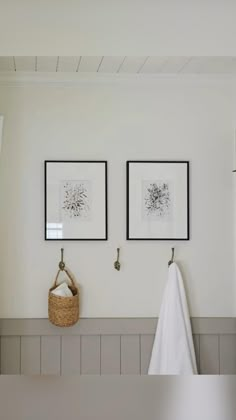 two framed pictures hang on the wall above a towel rack