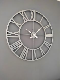 a large metal clock with roman numerals on the face is shown against a gray wall