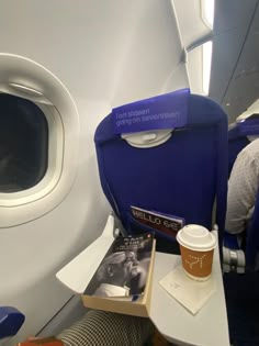 an airplane seat with a cup of coffee and magazine on the table next to it