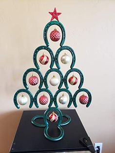 a christmas tree made out of ornaments on top of a black table with a white wall behind it