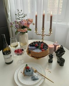 a table topped with a cake covered in fruit next to wine glasses and candles on top of it