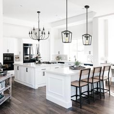 a large kitchen with white cabinets and wooden flooring, black chandelier hanging from the ceiling