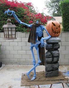 a blue skeleton statue holding a jack - o'- lantern on top of a cement block