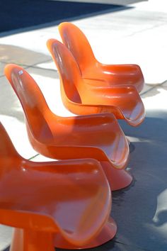 three orange plastic chairs sitting on top of a sidewalk