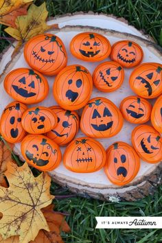 orange pumpkins with faces painted on them sitting in the grass next to fallen leaves