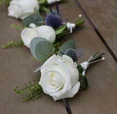 white roses and greenery are arranged on a wooden table for a bridal party