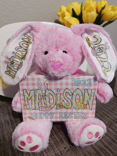 a pink stuffed rabbit holding a sign that says happy easter with flowers in the background