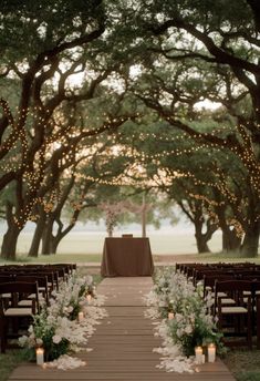 A wedding ceremony setup under a canopy of trees adorned with string lights. Wooden chairs line both sides of an aisle decorated with white flowers and candles, leading to an altar draped with fabric. The scene has a warm, romantic ambiance. Small Wedding Backdrop Ideas, Garden Simple Wedding, Private Intimate Wedding Ideas, Small Wedding Outside, Small Wedding Garden, Wedding Ideas Small Intimate, Small Christian Wedding, Classy Small Wedding, Small Ceremony Wedding