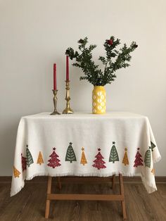 a table topped with a white table cloth covered in christmas trees and pine cones next to two candles