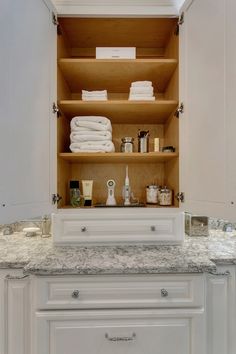 an open cabinet in the middle of a kitchen with white cabinets and marble counter tops