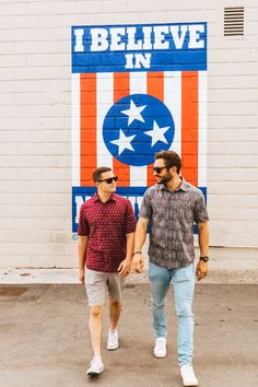 two men are walking in front of a sign that says i believe in american flag