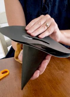 a woman holding a black hat on top of a wooden table next to a pair of scissors