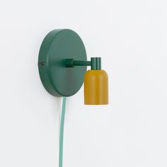 a green and yellow wall light next to a small bottle on a white wall with a cord