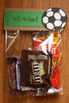 an assortment of snacks wrapped in plastic on top of a wooden table next to a soccer ball