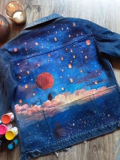 a denim jacket with hot air balloons painted on it and some paintbrushes next to it