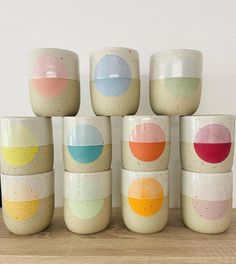 six cups with different designs on them sitting on a wooden table next to a vase