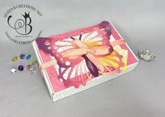 a pink and white box with a butterfly on the inside, surrounded by jewels in front of it