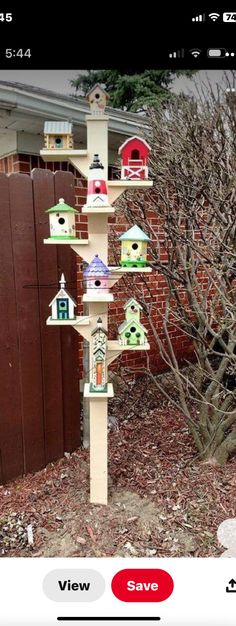 a tree with bird houses on it in front of a brick wall and fenced yard