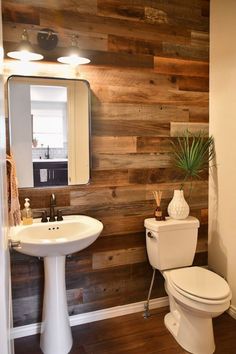 a white toilet sitting next to a sink in a bathroom under a wooden paneled wall