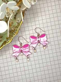 two pink bows and pearls are hanging from earrings on a table next to white flowers