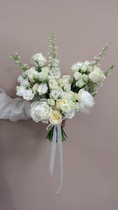 a bridal bouquet with white roses and greenery on a brides arm against a pink wall