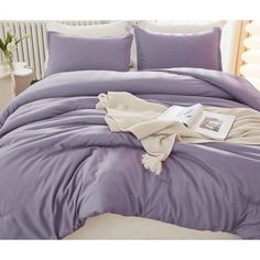 a bed with purple sheets and pillows on it