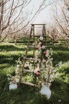 an old ladder is decorated with flowers and greenery for a wedding ceremony in the orchard