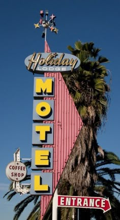 a motel sign with palm trees in the foreground and a blue sky behind it