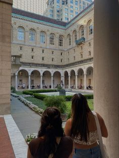 two girls are looking out the window at an old building with arches and courtyards