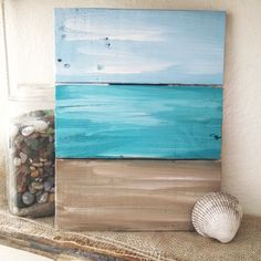 a seashell sits on a shelf next to an ocean scene painted in acrylic paint