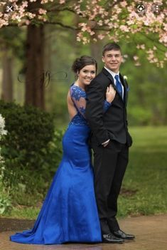 a young man and woman in formal wear posing for a photo under a flowering tree