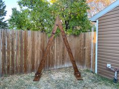 a wooden sculpture sitting in the middle of a yard next to a fence and tree