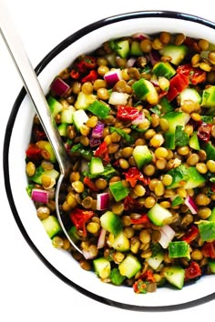 a white bowl filled with corn, cucumber and red onion salad next to a spoon