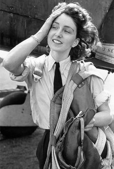 black and white photograph of a woman in uniform with an airplane on the ground behind her