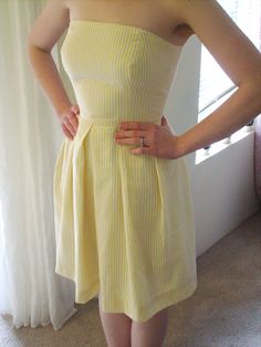 a woman wearing a yellow dress standing in front of a window with her hands on her hips